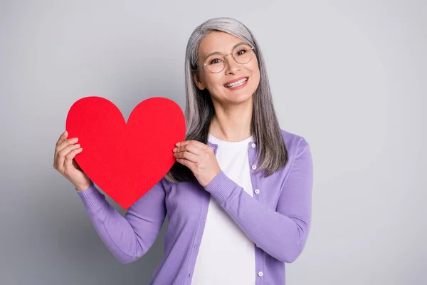 Foto retrato da avó segurando grande coração vermelho cut-out para o lado vestindo camisa violeta isolado em fundo de cor cinza — Fotografia de Stock