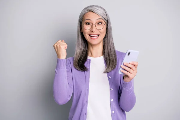 Foto ritratto di donna allegra che celebra la vittoria tenendo il telefono cellulare un pugno isolato su sfondo di colore grigio — Foto Stock