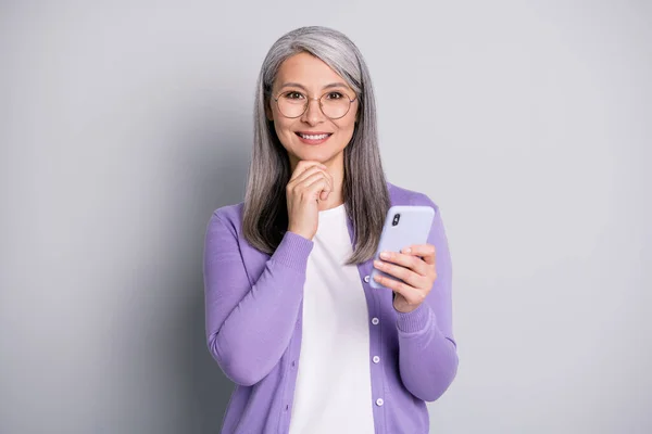 Foto ritratto di donna mentalità tenendo smartphone toccare mento con mano indossando camicia viola isolato su sfondo grigio — Foto Stock