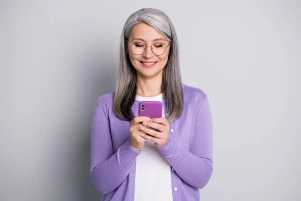 Портрет фото смарт-бабушки с помощью смартфона текстовый просмотр в очках улыбаясь изолированные на сером фоне цвета — стоковое фото