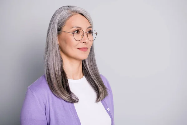 Портретное фото уверенной сконцентрированной опытной пожилой предпринимательницы в очках и фиолетовом кардигане, выделенном на сером фоне — стоковое фото