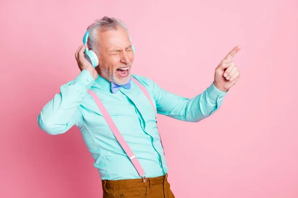 Портретне фото старого чоловіка, що слухає музику з навушниками, що співають улюблену пісню, вказуючи пальцем ізольовано на рожевому кольорі — стокове фото