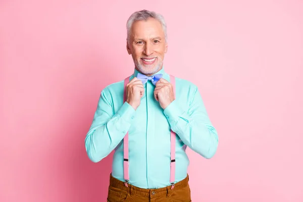 Fénykép portré idős férfi készül party öltöztetős kék csokornyakkendő rózsaszín póló nadrágtartó mosolygós elszigetelt rózsaszín háttér — Stock Fotó