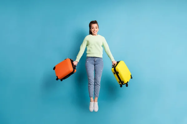 Tam boy vücut ölçülerinde, atlayan kızın havaalanındaki uçuş öncesi renkli bavullarını canlı mavi arka planda tutarken çekilmiş bir fotoğrafı. — Stok fotoğraf