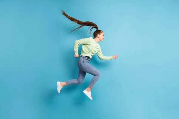 フル長さボディサイズサイドプロフィール写真のジャンプ実行中の急いで女の子とともに長い髪ponytail孤立した上の明るい青の色の背景 — ストック写真