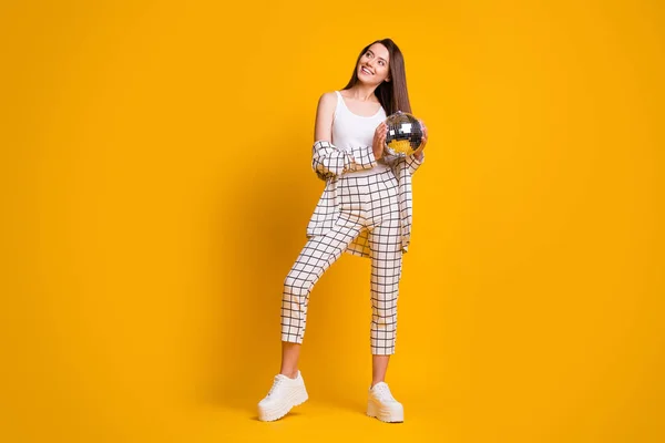 Full size foto van mooie schattige bruine haar meisje houden disco bal slijtage gecontroleerd pak witte tank-top schoenen geïsoleerd over gele achtergrond — Stockfoto