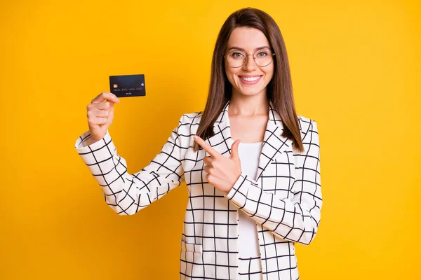 Retrato fotográfico de una alegre mujer de negocios apuntando con el dedo a una tarjeta bancaria de plástico aislada sobre un fondo de color amarillo vivo — Foto de Stock