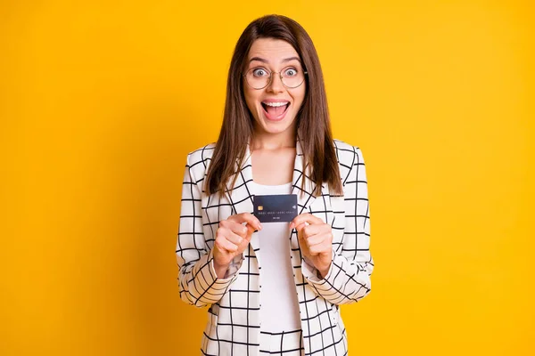 Foto retrato de la divertida chica asombrada mirando fijamente mantener la tarjeta de crédito con gafas aisladas en el fondo de color amarillo brillante — Foto de Stock