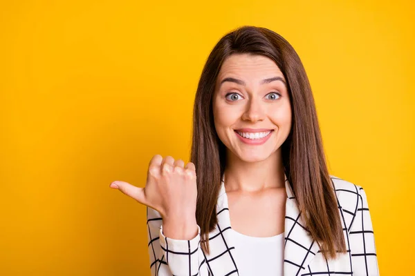 Foto de linda mujer alegre vestida de tartán blanco traje formal apuntando un dedo pulgar espacio vacío aislado color amarillo fondo — Foto de Stock