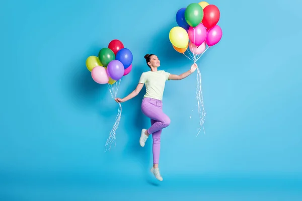 Full längd kropp storlek foto av barnslig flicka hoppar högt med högar av färgglada ballonger ler isolerad på pulserande blå färg bakgrund — Stockfoto