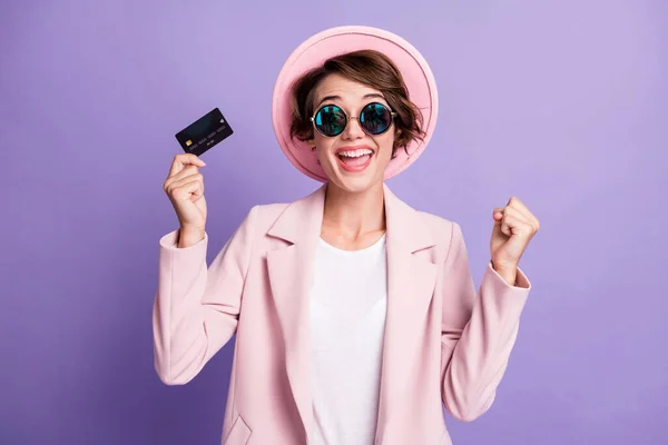 Fotografie kudrnaté štěstí žena nosit příležitostné růžové vinobraní blejzr brýle držení bezdrátové kreditní karty ruka paže pěst izolované fialové barvy pozadí — Stock fotografie