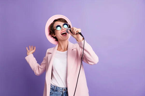 Foto de bonito pelo bob mujeres jóvenes usan gafas de abrigo de gorra cantando en micrófono aislado sobre fondo de color violeta —  Fotos de Stock