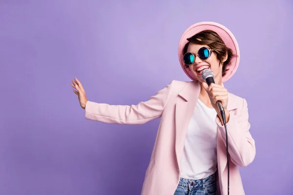 Foto de adorable pelo bob bonita joven dama usar gorra abrigo gafas cantando en micrófono aislado sobre fondo de color violeta — Foto de Stock