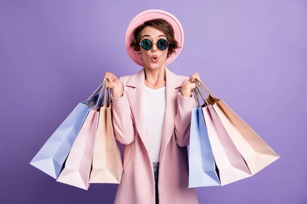 Retrato de animado positivo menina segurar muitos sacos fazer compras usar óculos rosa cap coat isolado sobre pastel cor roxa fundo — Fotografia de Stock