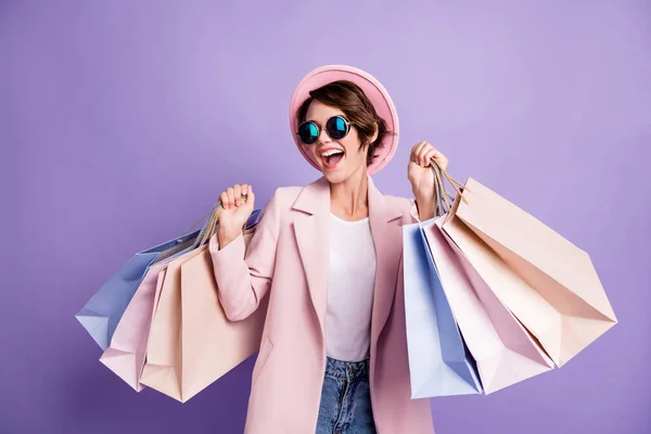 Foto de la joven morena bastante optimista sorprendida hacer compras usar gafas capa gorra rosa aislado sobre fondo de color púrpura —  Fotos de Stock