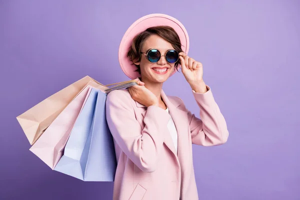 Портрет чарівної солодкої брюнетки волосся молода леді тримає сумки дотик окуляри носити рожеве шапочка пальто ізольовано на фіолетовому кольоровому фоні — стокове фото