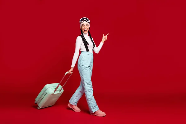 Foto em tamanho completo de jovem menina feliz animado com caudas ir segurar o dedo do ponto de bagagem copyspace isolado no fundo cor vermelha — Fotografia de Stock