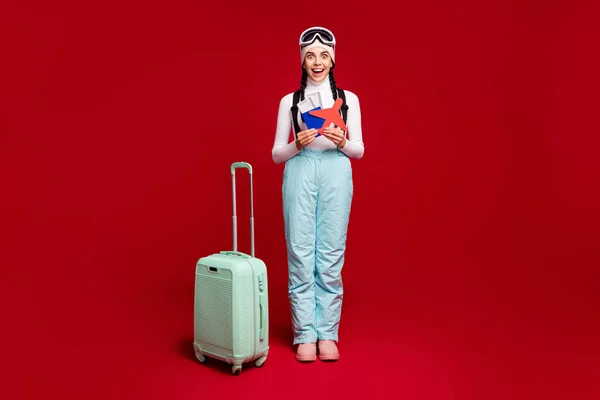 年轻兴奋的女孩拿着护照，红色纸飞机穿着蓝色裤子，与红色背景隔离的全副照片 — 图库照片