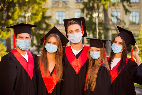 Fotoportret van vijf afgestudeerden in gewaden en hoeden met kwastje die gezichtsmaskers dragen en elkaar knuffelen — Stockfoto