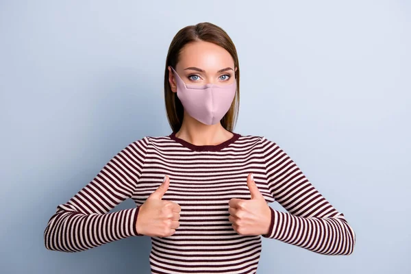 Portret van een charmant mooi meisje in roze stof gezichtsmasker met twee duimen omhoog kijkend naar camera geïsoleerd op grijze achtergrond — Stockfoto