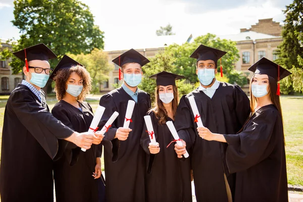 Foto retrato de seis graduados mostrando diplomas usando máscaras no exterior — Fotografia de Stock