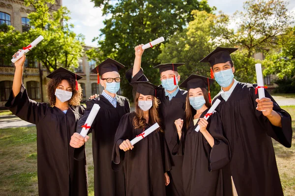 Portrait photo de six étudiants célébrant la remise des diplômes avec des mains portant des masques à l'extérieur — Photo