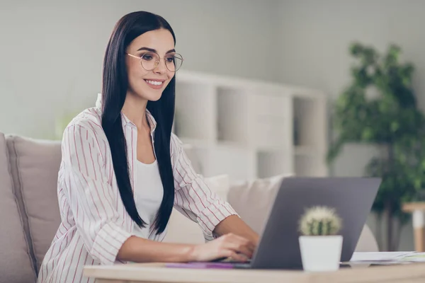 Photo de jeune femme confiante assis confortable canapé mains ordinateur portable porter des lunettes chemise dans le bureau à la maison à l'intérieur — Photo