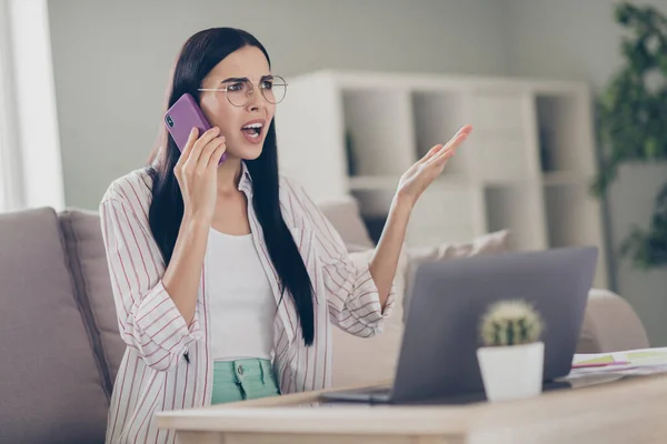 Fotografie mladé pobouřené obchodní dáma držet telefon argument nosit brýle košile v domácím pracovišti indoors — Stock fotografie