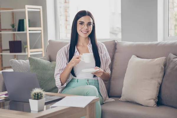 Фото молодой деловой женщины сидеть диван держать чашку напитка расслабления носить очки рубашку в домашней рабочей станции в помещении — стоковое фото