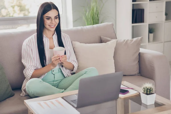 Foto de retrato de una joven trabajadora usando un portátil en casa sonriendo manteniendo la taza con bebida caliente usando anteojos leyendo — Foto de Stock