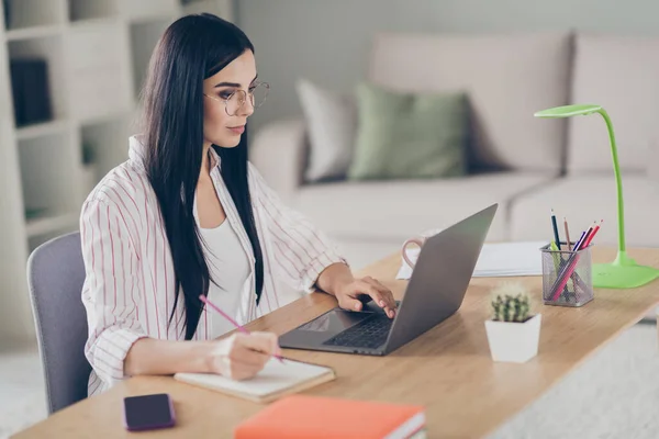 Retrato fotográfico de una mujer de negocios concentrada y reflexiva que utiliza la computadora navegando por Internet tomando notas con pluma — Foto de Stock