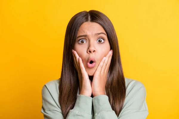 Foto de impactada niña impresionada vestida casual verde traje brazos mejillas ojos grandes aislado color amarillo fondo — Foto de Stock