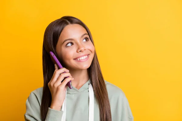 Foto de adorável positivo escola menina desgaste casual cinza roupa falando moderno gadget olhando espaço vazio isolado cor amarela fundo — Fotografia de Stock