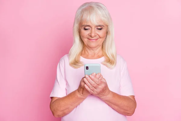 Akıllı telefon kullanarak gülümseyen sevimli büyükannenin fotoğrafı. Pastel pembe arka planda izole edilmiş gülümsüyor. — Stok fotoğraf