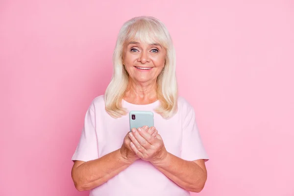 Hoş bir büyükannenin portresi cep telefonlarını internette gezdirirken pastel pembe arka planda izole edilmiş gülümsüyor. — Stok fotoğraf