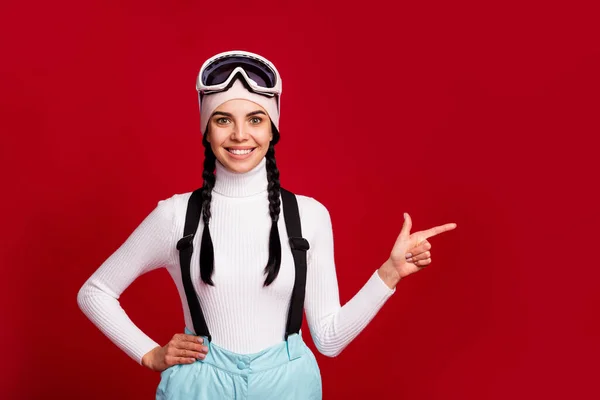 Foto di giovane bella attraente sorridente positivo ragazza sciatore punto dito copyspace raccomandare resort isolato su sfondo di colore rosso — Foto Stock