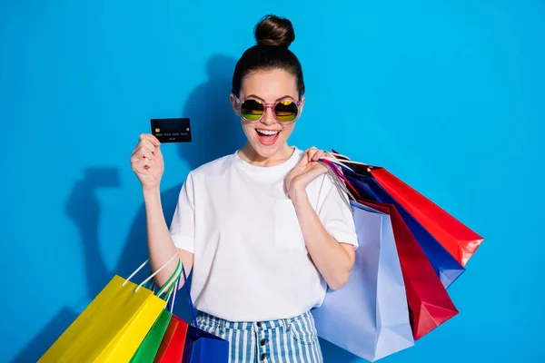 Porträtt av positiva chockad flicka njuta av betala köp plast bankkort hålla många påsar bära vit t-shirt randig jeans jeans isolerad över ljusa glans färg bakgrund — Stockfoto