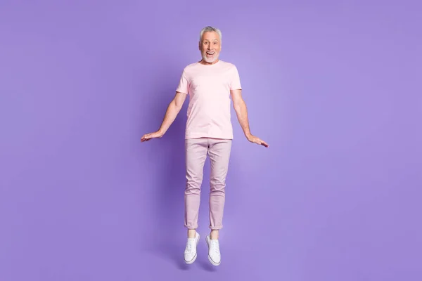 Full length φωτογραφία του γέρου άλμα παιδαριώδη παλάμες φορούν ροζ t-shirt παντελόνι sneakers απομονωμένο βιολετί χρώμα φόντο — Φωτογραφία Αρχείου