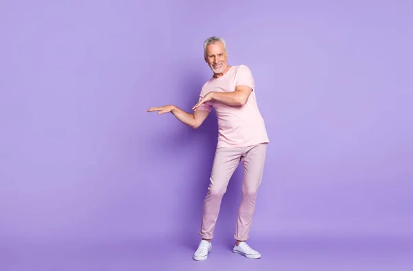 Emekli yaşlı adamın tam boy fotoğrafı dans kolları pembe t-shirt pantolon giyerek izole edilmiş mor arka plan. — Stok fotoğraf