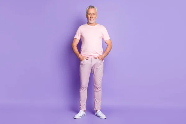 Фото уверенного деда руки карманы зубастый блестящая улыбка носить розовые кроссовки футболки брюки изолированные фиолетовый цвет фона — стоковое фото