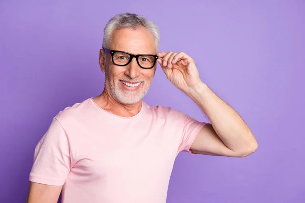 Фото пенсионера дедушки держать спецификации смотреть камера улыбается носить очки розовые футболки изолированы фиолетовый цвет фона — стоковое фото