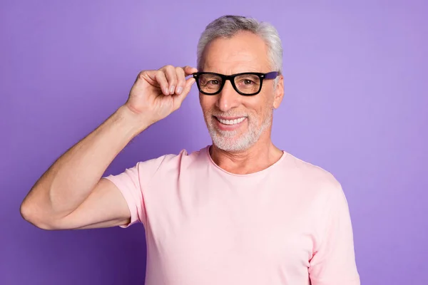 Foto av pensionerad farfar hålla glasögon strålande leende bära glasögon rosa t-shirt isolerad violett färg bakgrund — Stockfoto