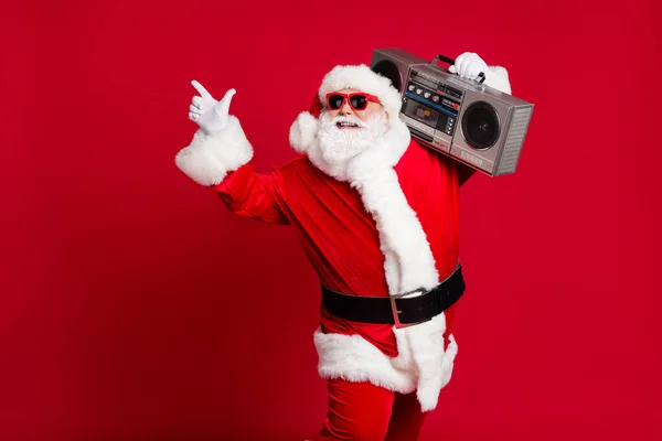 Hip-hop cud. Pełna długość zdjęcie emeryta starzec szary broda uśmiech trzymać boombox bezpośredni palec puste miejsce nosić Santa X-mas kostium okulary przeciwsłoneczne odizolowane czerwony kolor tło — Zdjęcie stockowe