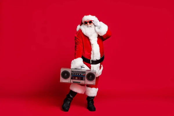Pełna długość zdjęcie emeryta stary człowiek szara broda śmieszne pozowanie trzymać okulary boom box nosić Santa rękawice płaszcz pasek okulary czarne buty odizolowany czerwony kolor tło — Zdjęcie stockowe