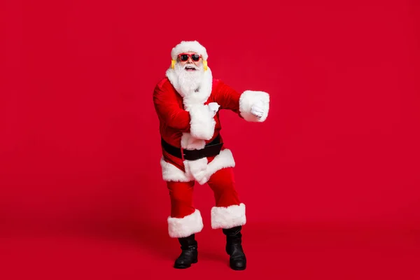 Emekli yaşlı adamın tam boy fotoğrafı gri sakal dansı komik el hareketi Noel Baba x-mas kostüm eldiven ceket güneş gözlüğü kulaklık siyah botlar izole edilmiş kırmızı arka plan — Stok fotoğraf