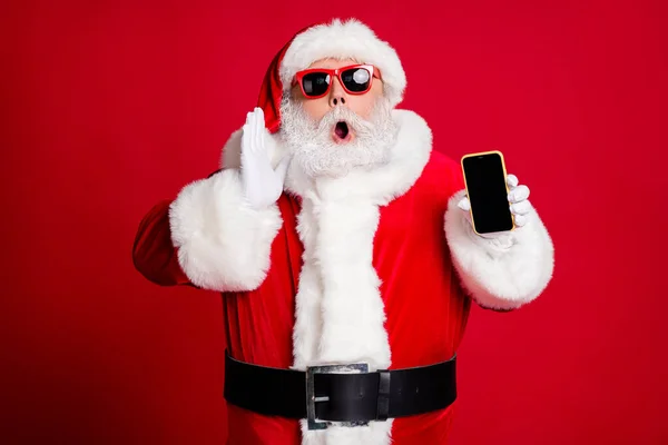 Photo de retraité vieil homme barbe grise tenir téléphone espace vide main bouche ouverte crier vente informations porter x-mas santa costume gants manteau ceinture lunettes de soleil chapeau isolé couleur rouge fond — Photo