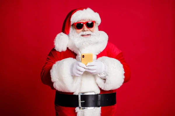 Portrait de son il beau beau concentré joyeux Père Noël barbu en utilisant l'appareil 5g blogging dactylographie félicitations boutique d'applications en ligne isolé lumineux vif éclat vibrant fond de couleur rouge — Photo
