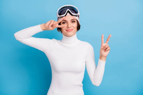 魅力的な若い女性の写真ショーvサイン良い気分冬の季節のスキーヤーは青の色の背景に隔離された — ストック写真