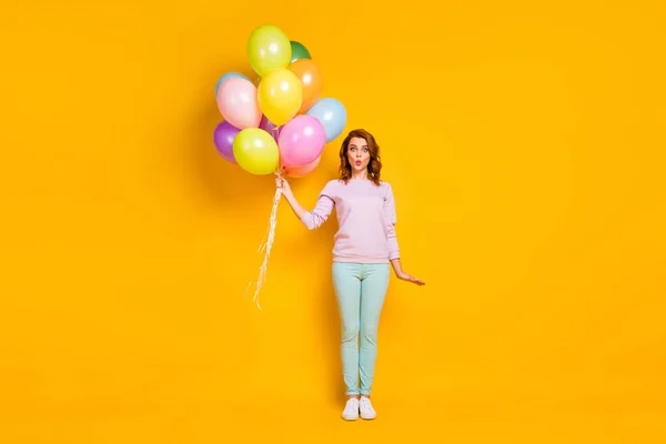 Foto de longitud completa de la mujer divertida sorprendida disfrutar de celebración festiva aniversario muchos globos envían aire beso desgaste traje de moda jersey aislado sobre fondo de color amarillo — Foto de Stock