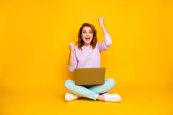 Full body photo ecstatic excited funy woman sit legs crossed work laptop win online lottery raise fists scream yeah wear turquoise pink pullover pants sneakers isolated yellow color background